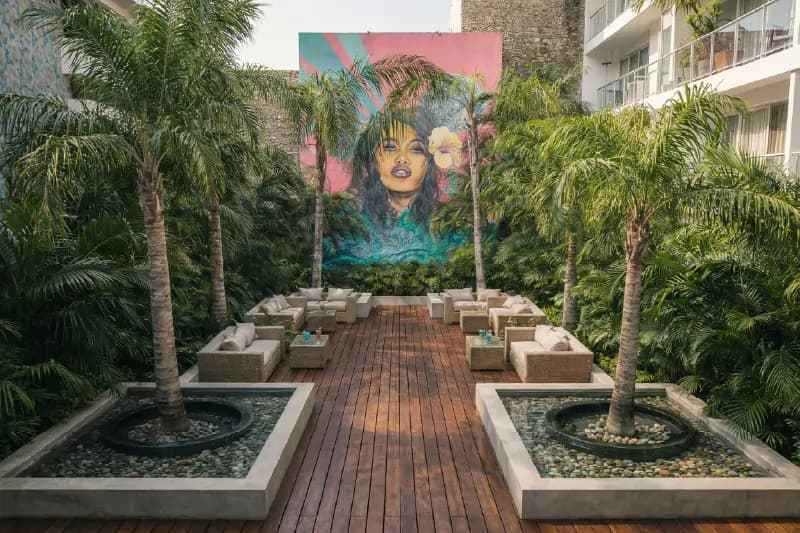 Patio interior con mobiliario de mimbre, palmeras y un mural artístico de una mujer al fondo.