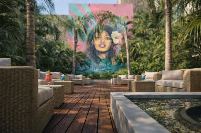 Cócteles sobre mesa de mimbre en patio tropical con vegetación densa y mural colorido.